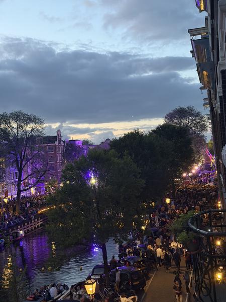 This photo captures a vibrant evening scene along the Prinsengracht in Centrum, Amsterdam, where a large crowd has gathered for what appears to be a lively festival or public event